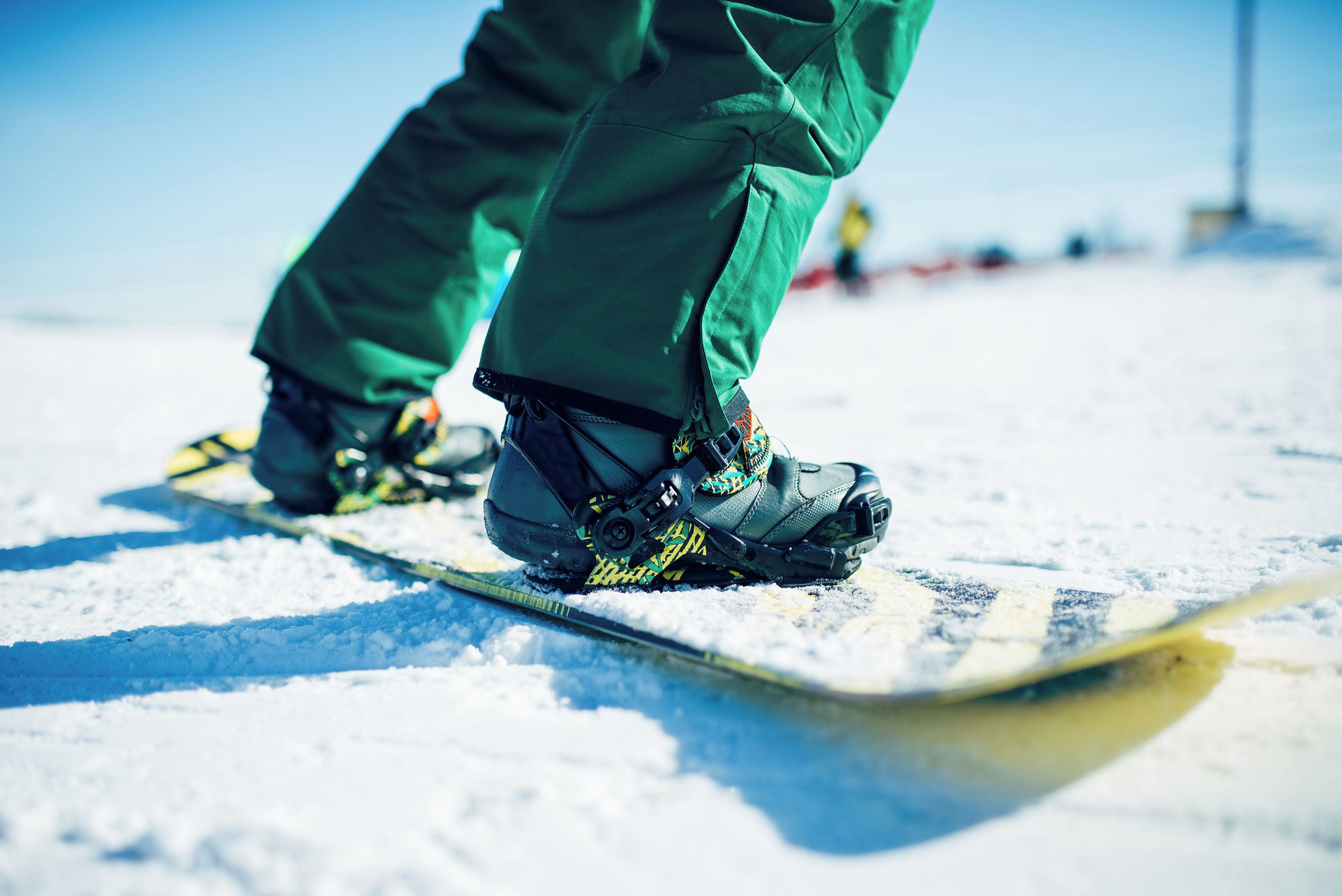 Ein Snowboarder mit grüner Hose und schwarzen Stiefeln auf einem Snowboard.