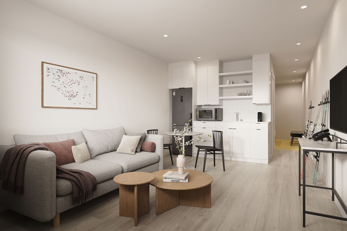 A modern living room with a grey sofa, two round wooden tables, and a kitchen in the background.