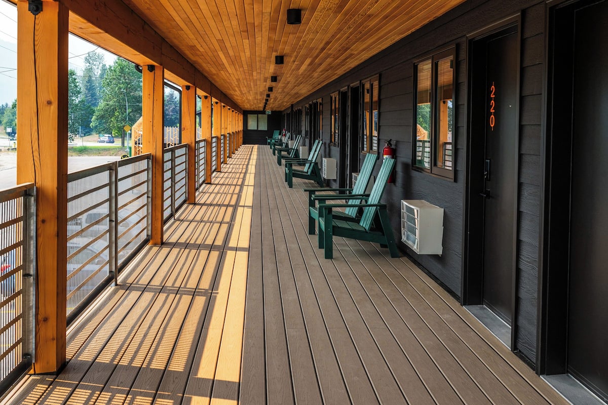A covered outdoor area with wooden flooring, green chairs, and a row of windows along the side.