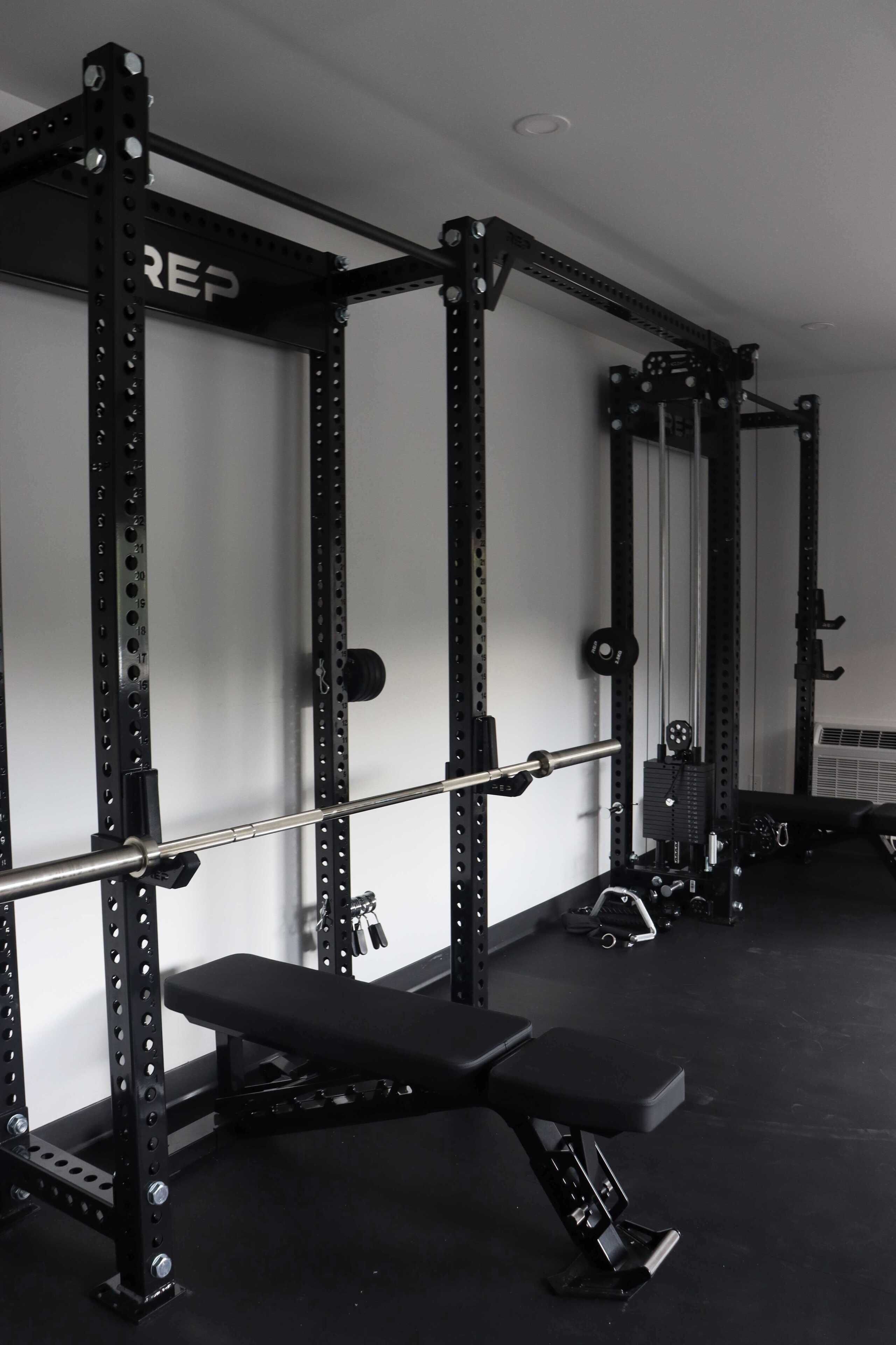 Een sportschool met een rack voor squats, een bank en gewichtsschijven.