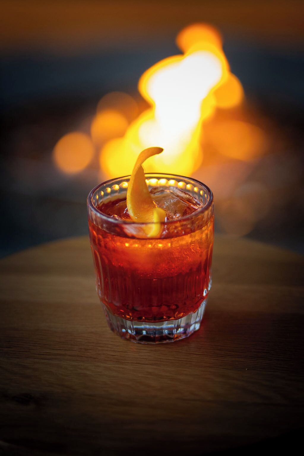 A glass of red beverage with a lemon slice garnish on a wooden surface.