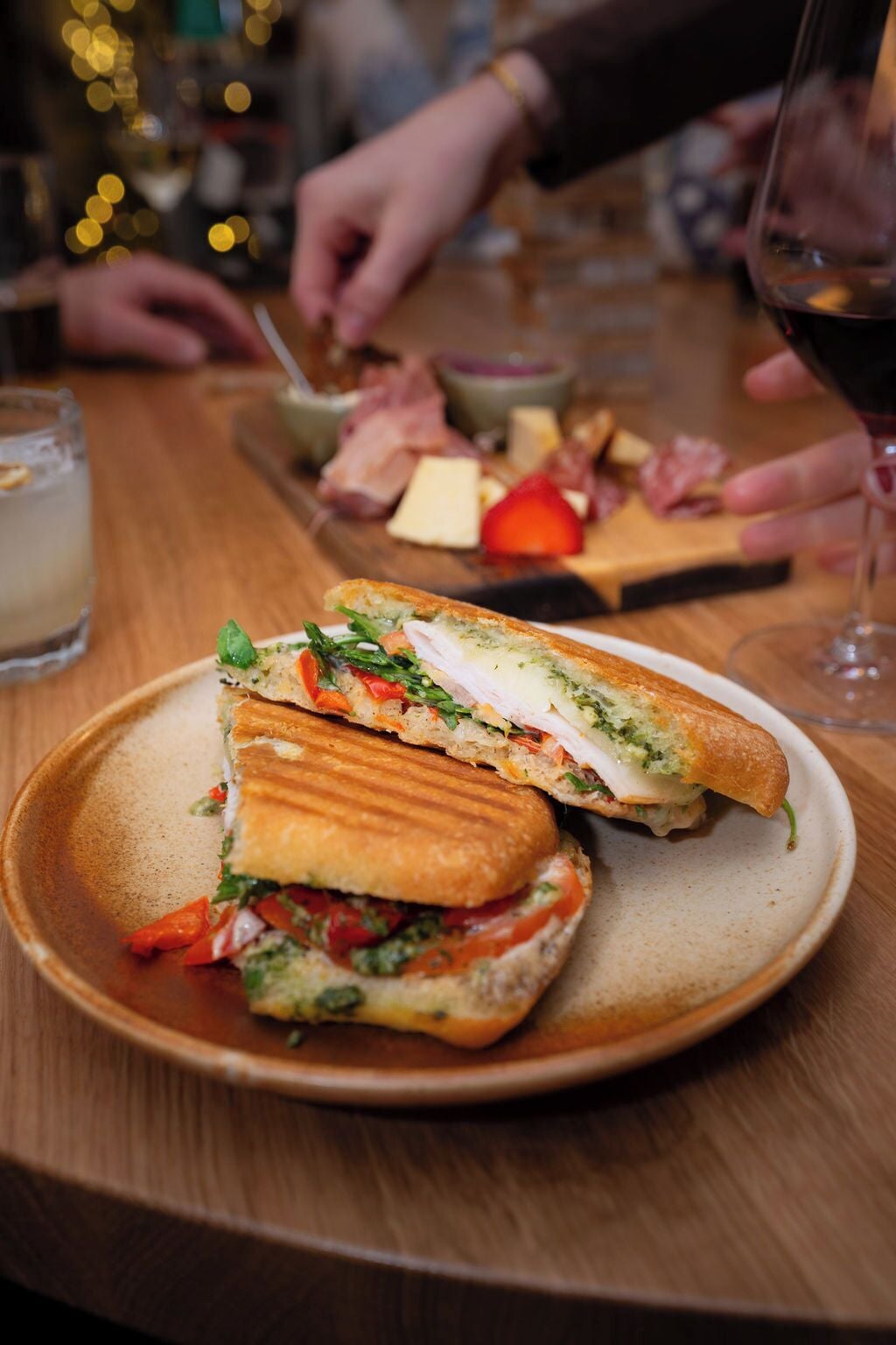 En sandwich på en tallerken med et træbord og et glas rødvin i baggrunden.