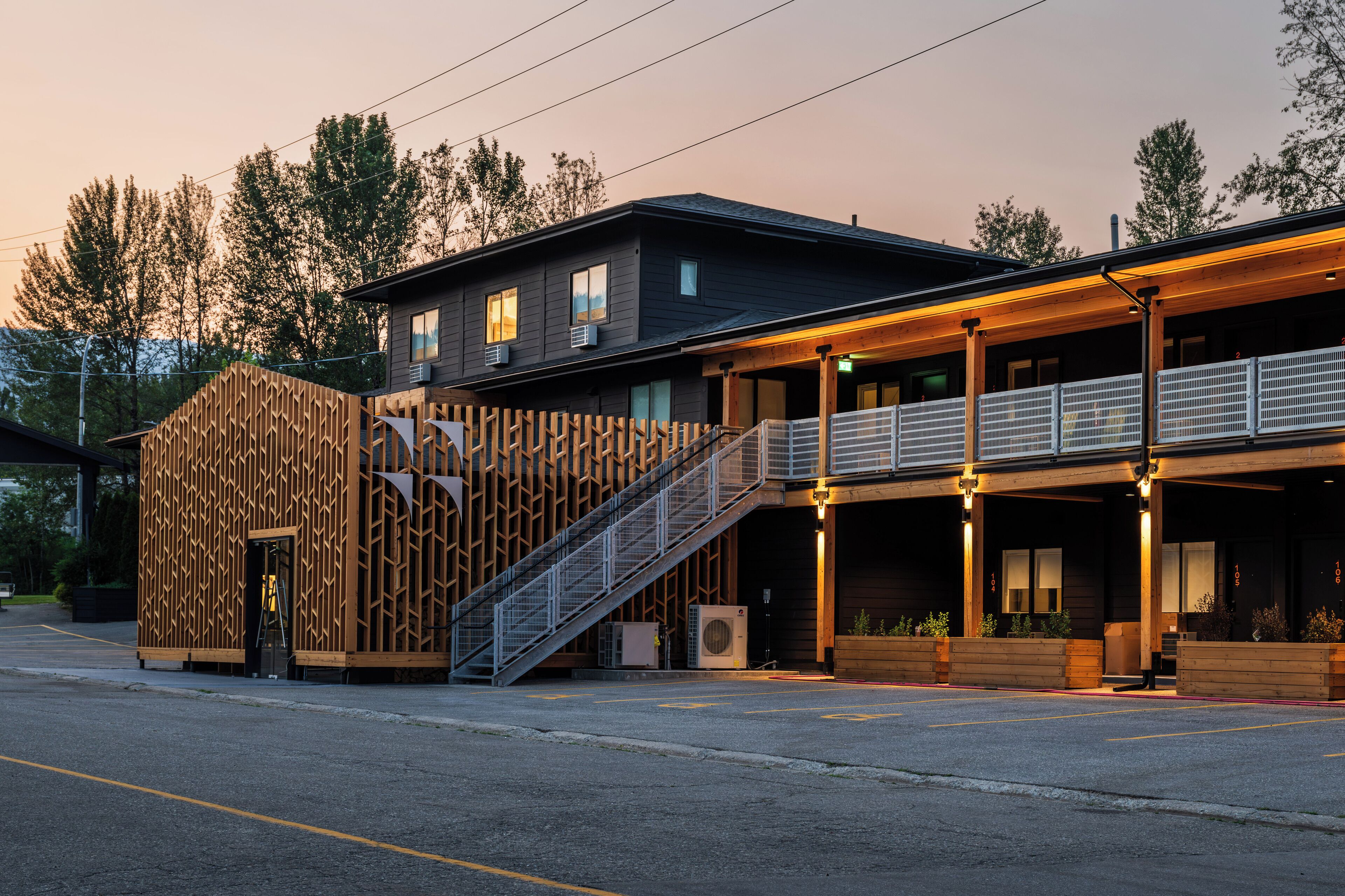 A modern building with a wooden facade, a covered outdoor seating area, and a staircase leading to the entrance.