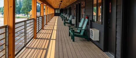 Un espace extérieur abrité, doté d’un plancher en bois, de chaises vertes et d’une rambarde.