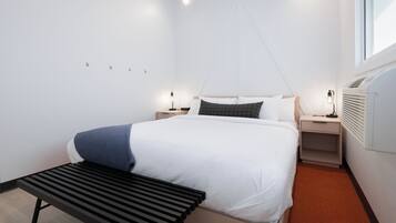 Une chambre d’hôtel moderne avec un grand lit, des tables de chevet, un banc et une fenêtre.