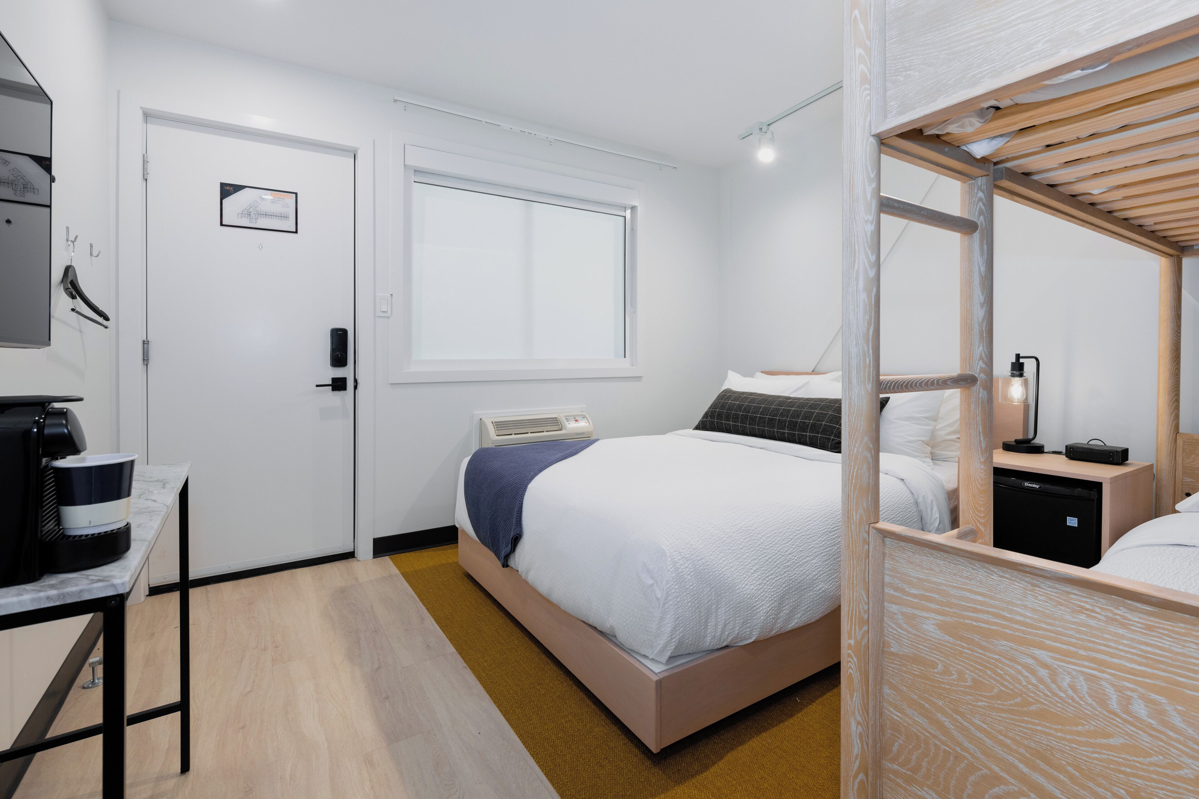 Una habitación de hotel moderna con cama, mesita de noche y un pequeño escritorio con cafetera.