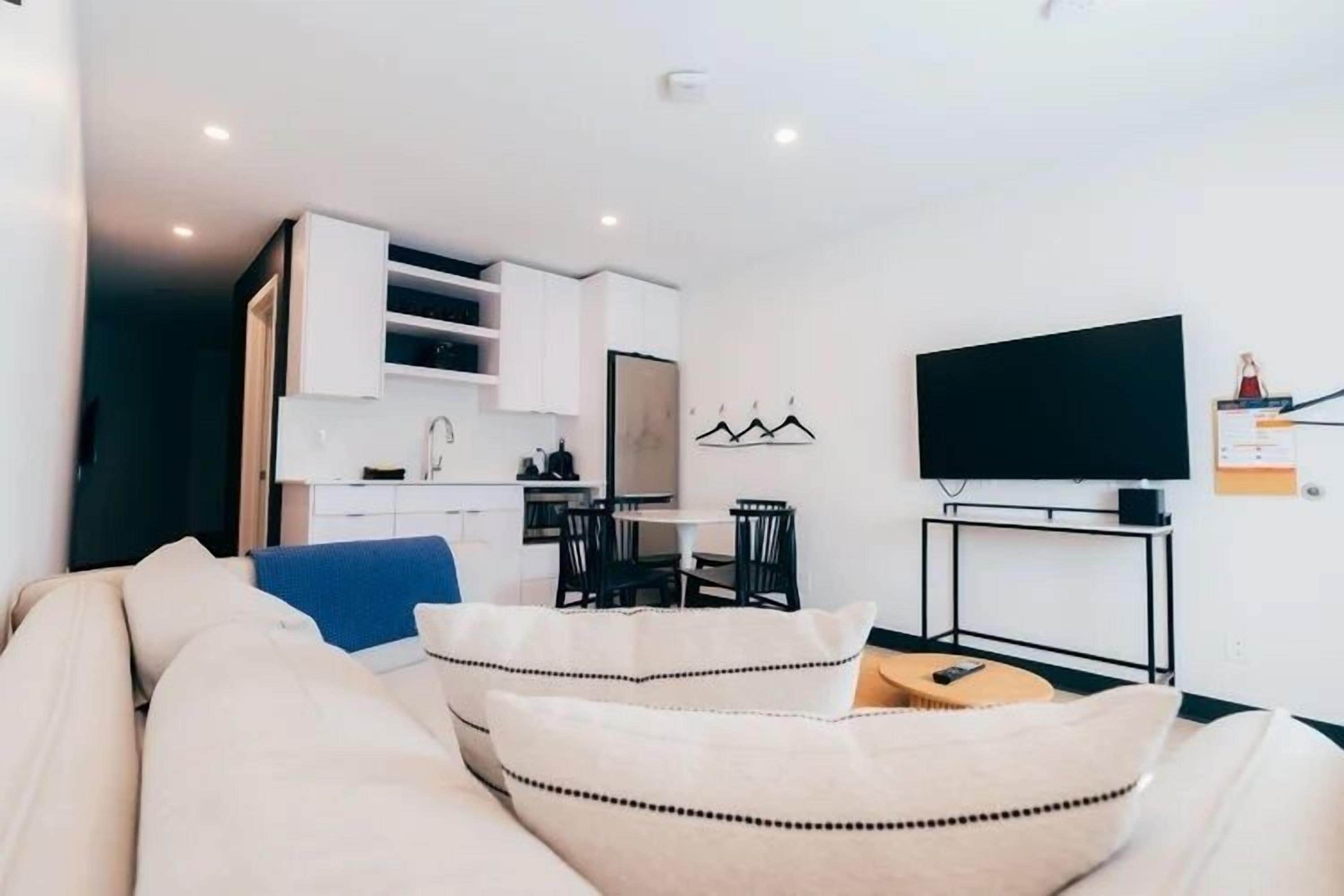 A modern living room with a sofa, a television, and a kitchen area in the background.