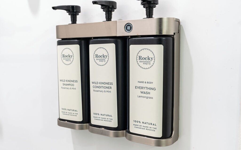 Un distributeur de savon mural contenant trois flacons étiquetés « Rocky Mountain Soap Co. ».