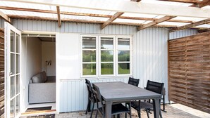 Un patio cubierto con mesa y sillas, una ventana con persianas y una valla de madera.