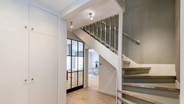 A modern interior with a staircase, wooden flooring, and a view into another room.
