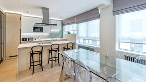 A modern kitchen with a central island, bar stools, and a glass dining table.