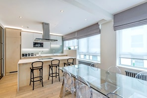A modern kitchen with a central island, bar stools, and a glass dining table. - The Buckingham & Lloyds Apartment (London)