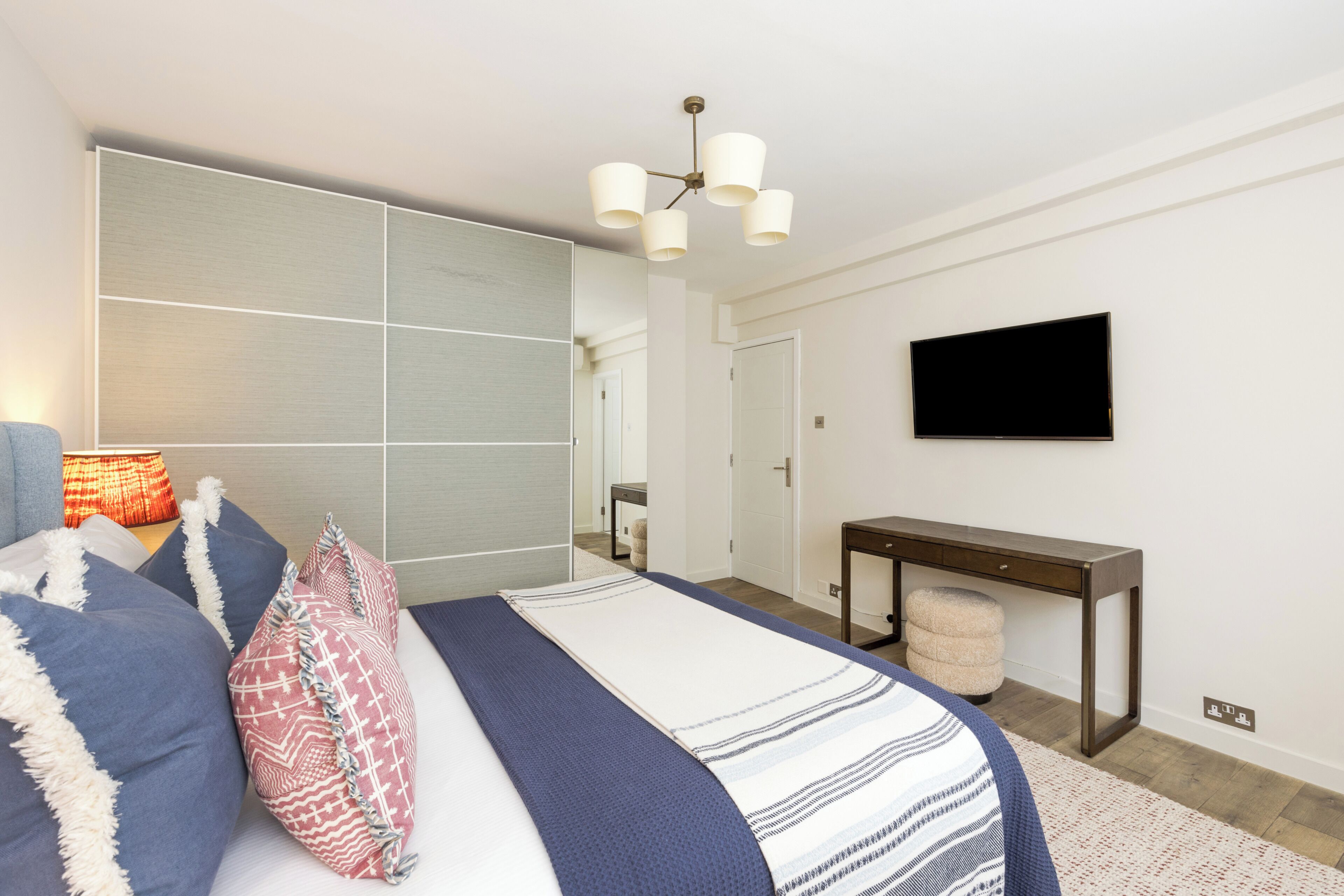 A modern bedroom with a bed, bedside lamp, and a TV mounted on the wall.