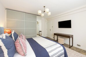 A modern bedroom with a bed, bedside lamp, and a flat-screen TV mounted on the wall. - Elegant Kensington Apartment · Hyde Park · Sleeps 4 (London)