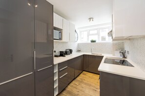 A modern kitchen with grey cabinets, a microwave, and a sink. - Elegant Kensington Apartment · Hyde Park · Sleeps 4 (London)