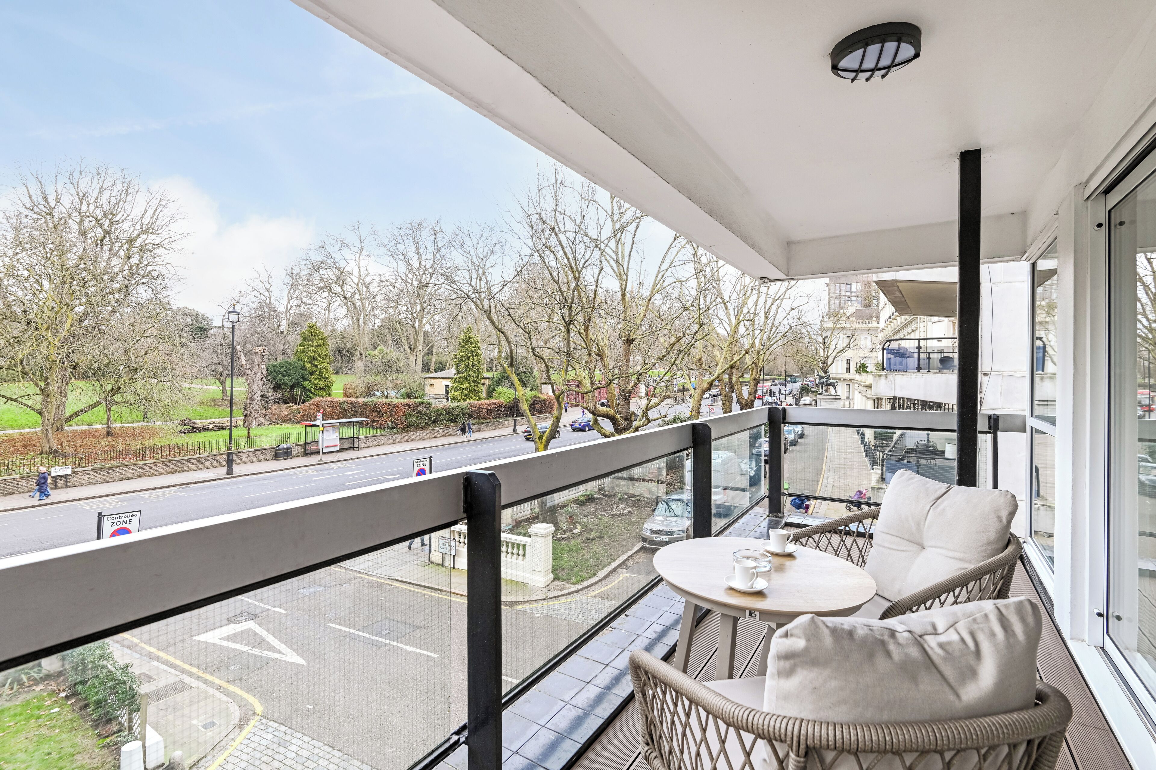 A balcony with wicker furniture and a view of a city street and park.