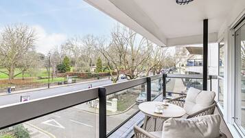 A balcony with wicker furniture and a view of a city street and park.
