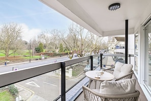 Un balcón con muebles de mimbre y vistas a una calle y un parque de la ciudad.
