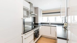 A modern kitchen with white cabinetry, stainless steel appliances, and a window providing natural light. - Stylish Kensington Apartment with Hyde Park View Terrace · Sleeps 4 (London)