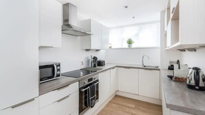 Una cocina moderna con armarios blancos, extractor de acero inoxidable, microondas, horno, pileta y una ventana con una planta.