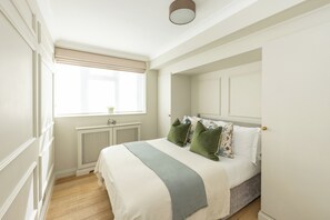 Une chambre avec un grand lit, une fenêtre avec des stores, un radiateur et une porte.