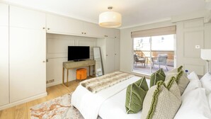 Un dormitorio con cama, televisor, escritorio y ventana con vistas al exterior.