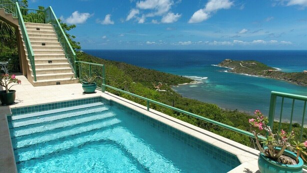 Ein Pool mit Stufen zum Wasser, umgeben von viel Grün und mit Blick auf die Küste.