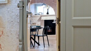 Ein Zimmer mit Steinwand, einem runden Spiegel und Blick in einen Küchenbereich mit Tisch und Stühlen.
