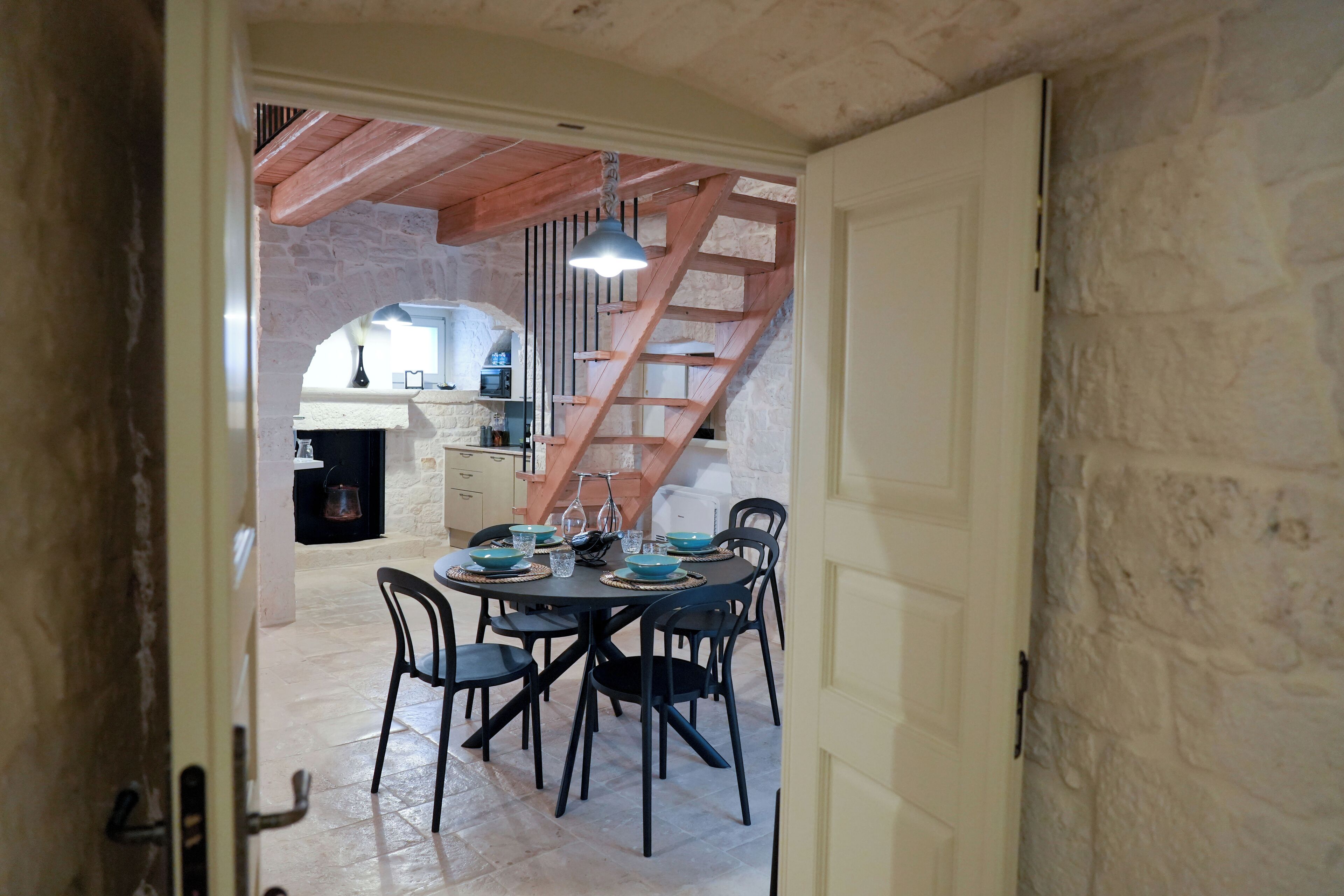 A dining area with a table set for four, a staircase, and a kitchen in the background.