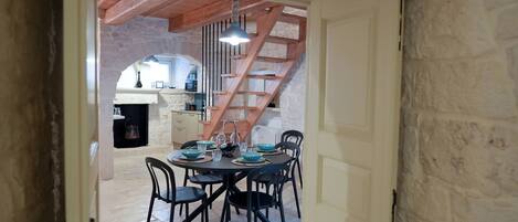 A dining area with a table set for four, a staircase, and a kitchen in the background.