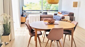 Un salon moderne avec une table à manger ronde en bois, des chaises rembourrées, un canapé et une grande fenêtre donnant sur un paysage verdoyant.