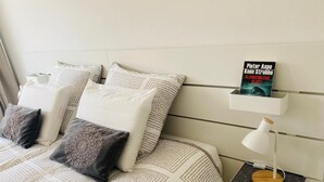 Un lit bien fait, avec une literie à motifs et des oreillers, une table de chevet avec une lampe, et un livre intitulé « Pieter Aspe Koen Stobbe » sur une étagère.