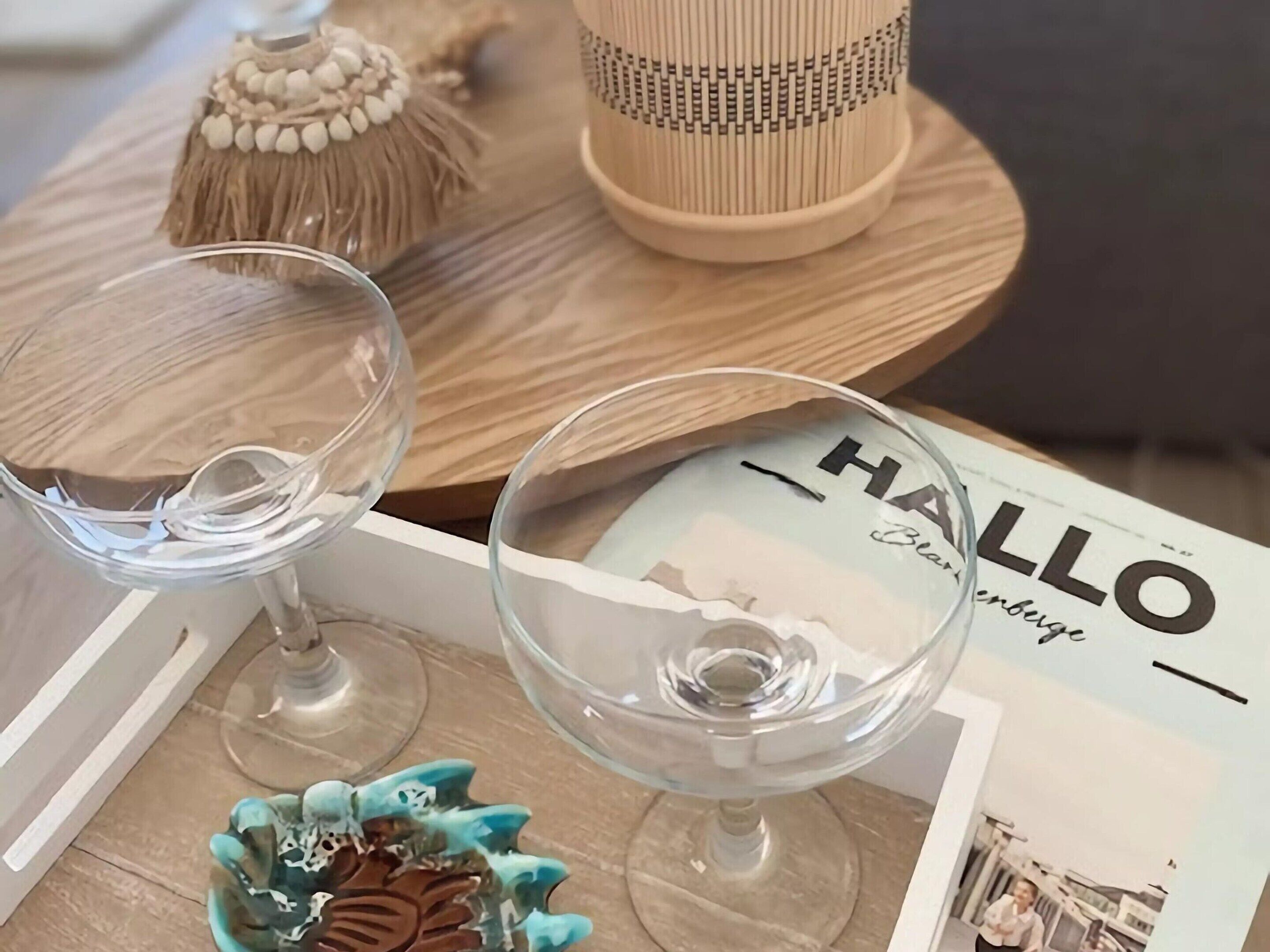 A magazine titled 'HALLO' on a wooden table with two clear glass wine glasses and a decorative ceramic bowl.