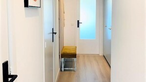 Un couloir étroit avec un banc, une porte dotée d’un panneau en verre dépoli et un tableau encadré accroché au mur.