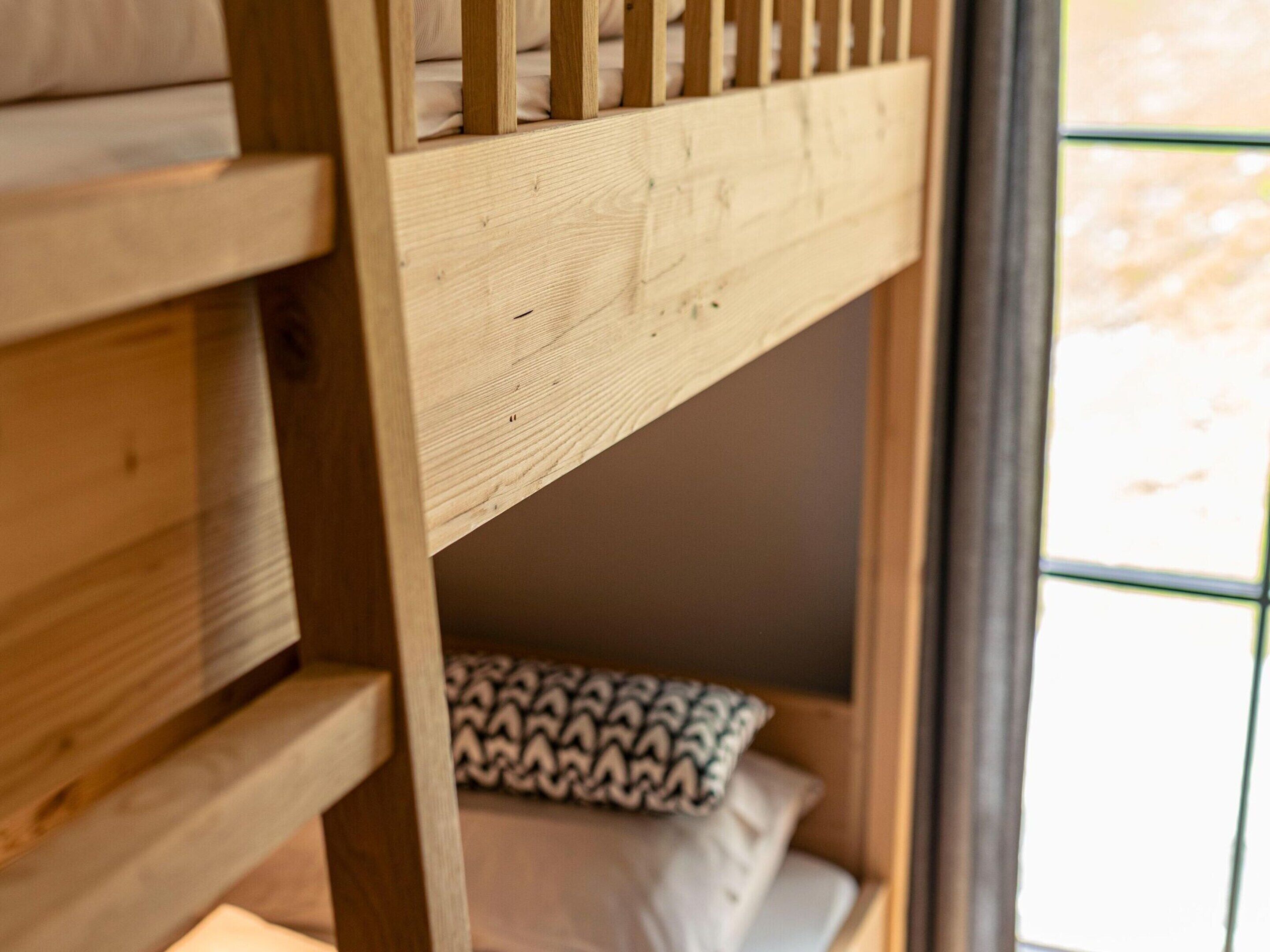 A wooden bunk bed with a patterned pillow and a window in the background.