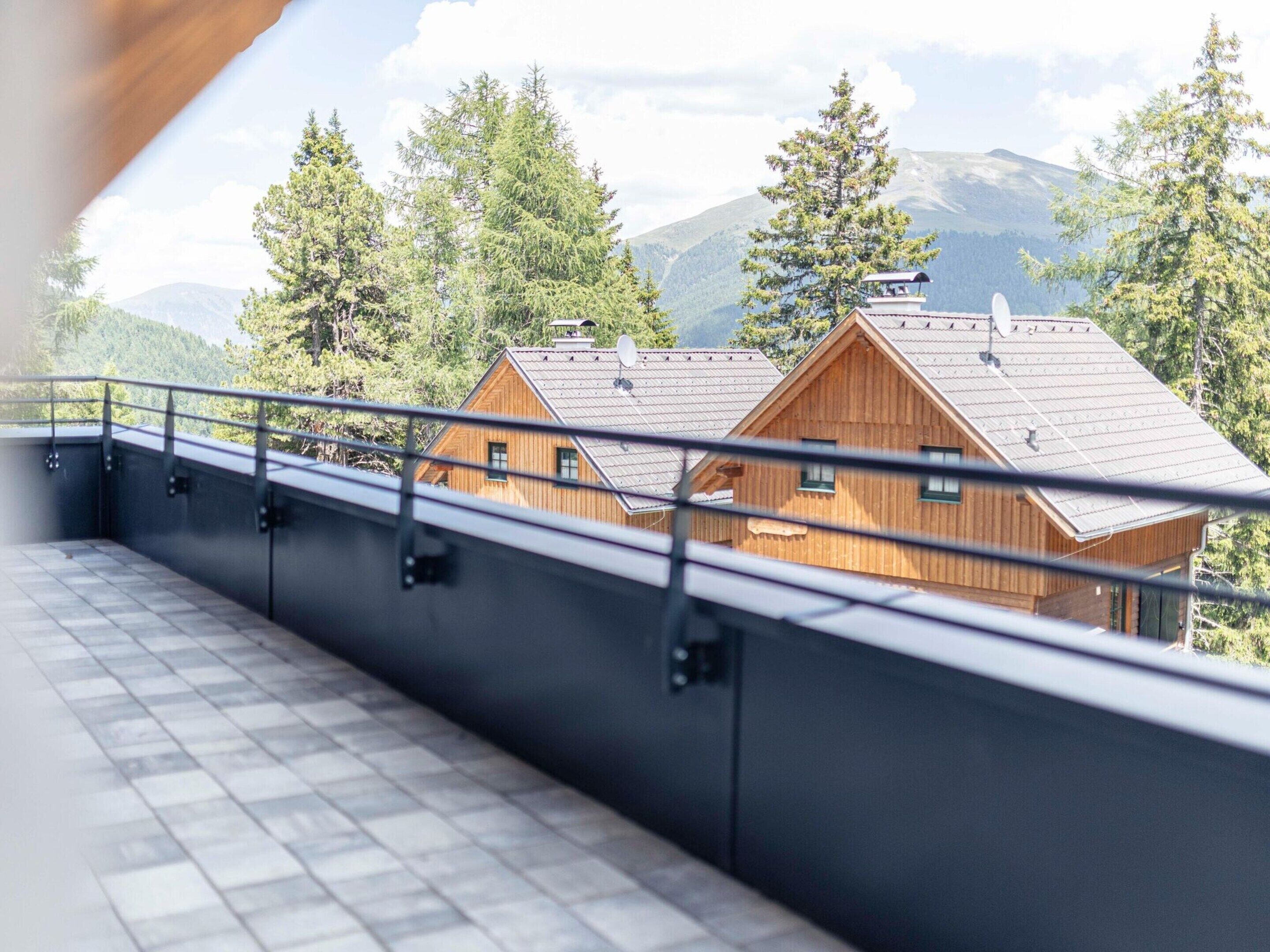 A wooden cabin with a metal roof, surrounded by trees and mountains.