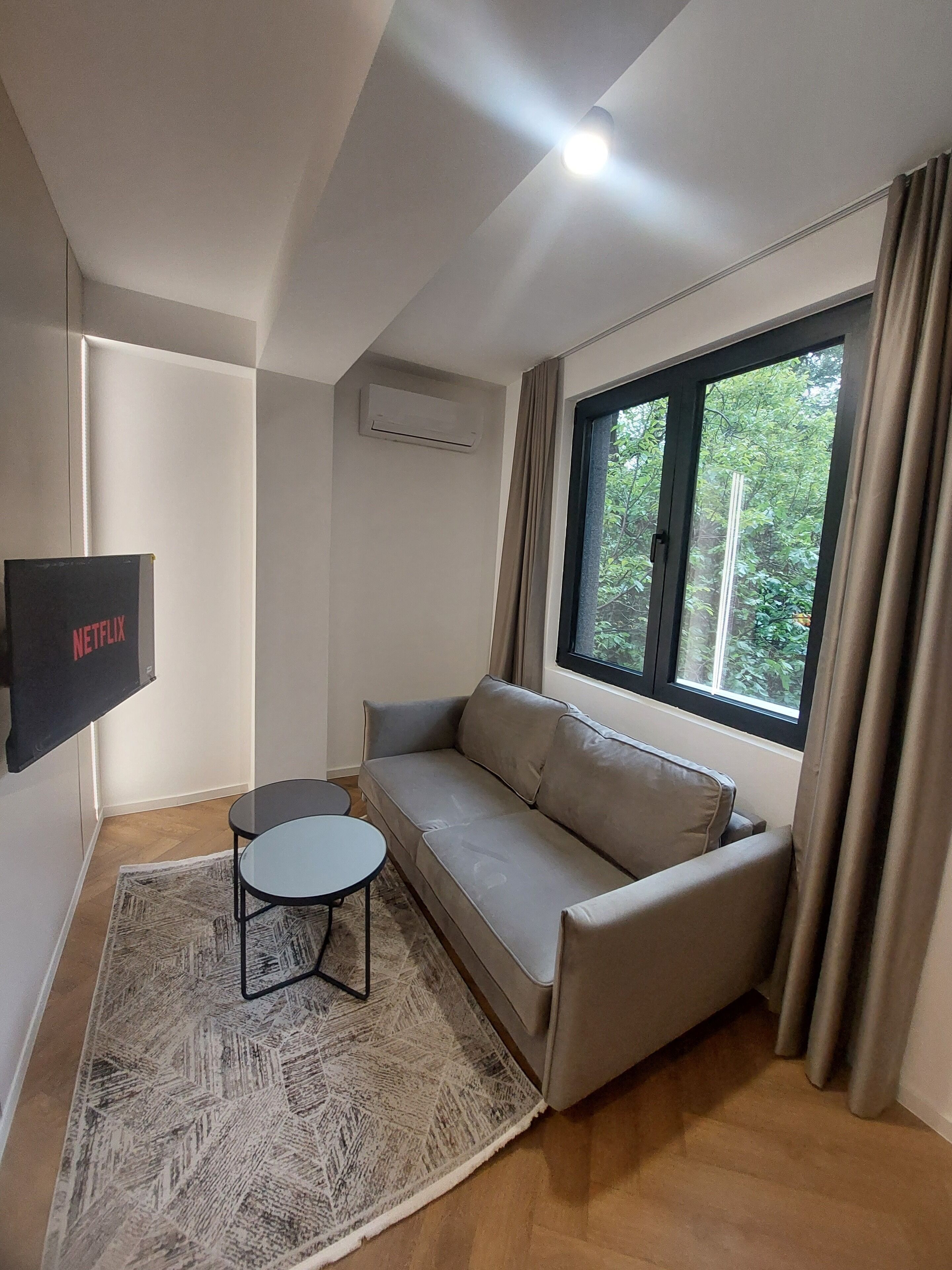 Una sala de estar moderna con un sofá color beige, una mesita redonda y un televisor montado en la pared.