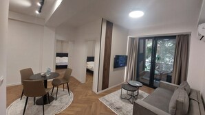 A hotel room with a dining area, a sofa, a TV, and a window with curtains.