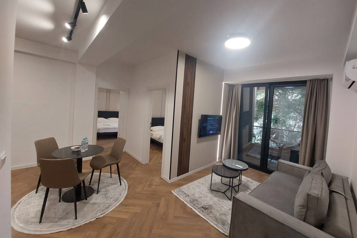 A hotel room with a dining area, a sofa, a TV, and a window with curtains.