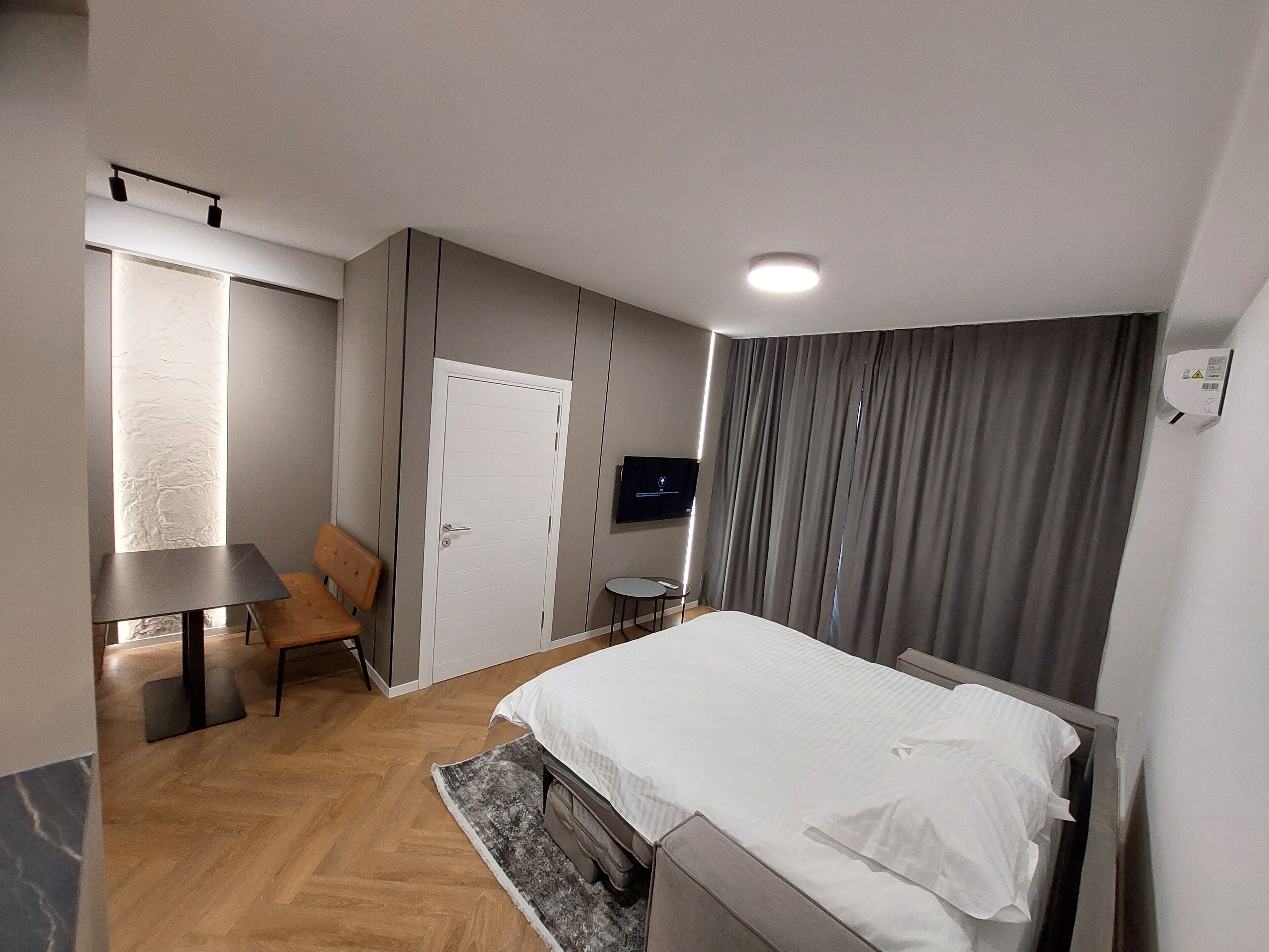 A modern hotel room with a large bed, a desk, a chair, a TV, and a window with curtains.