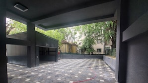 An outdoor area with a tiled floor, a red hose, and a building with a large open door.