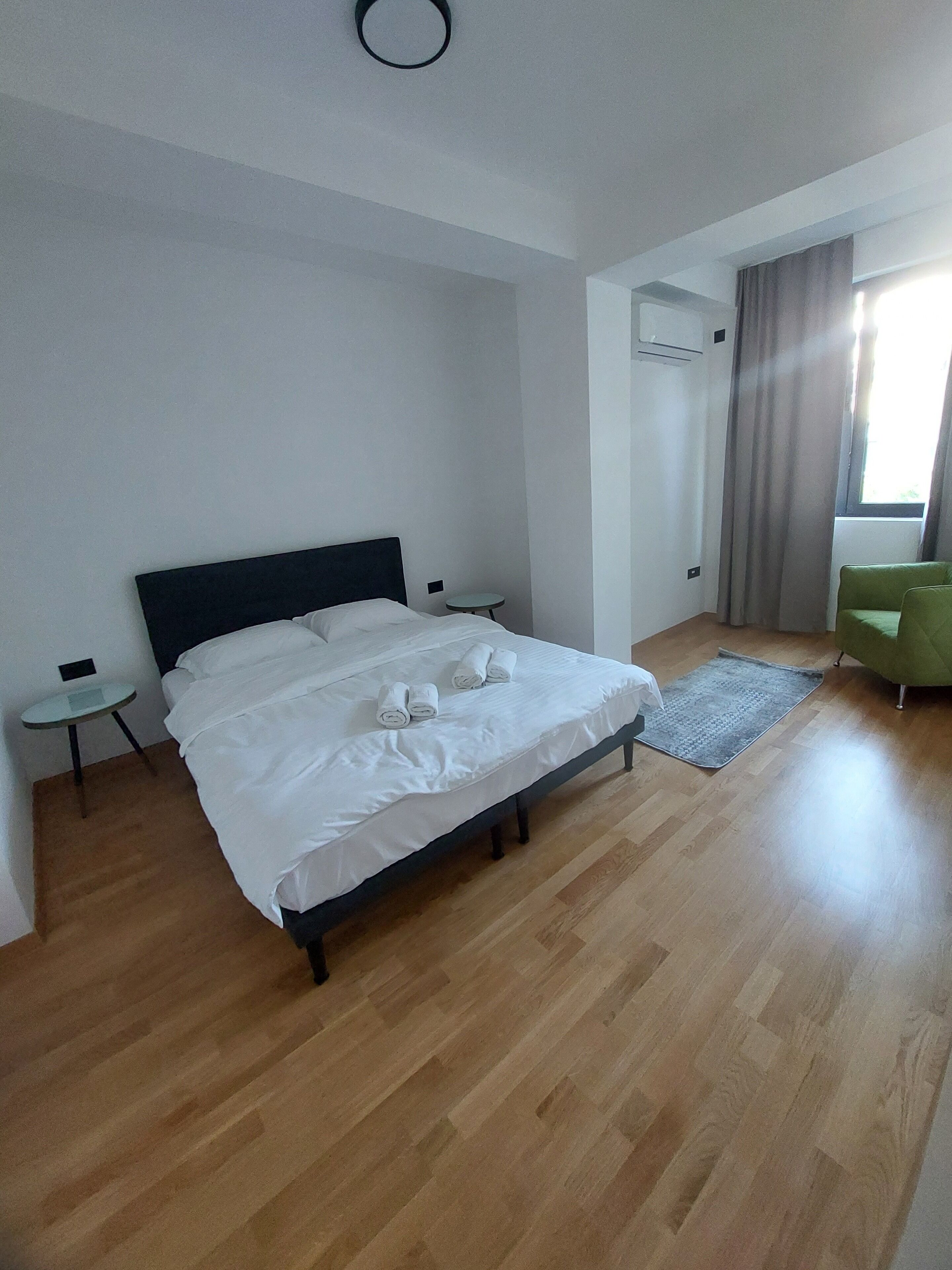 A bedroom with a bed, a small table, a chair, and a window with curtains.