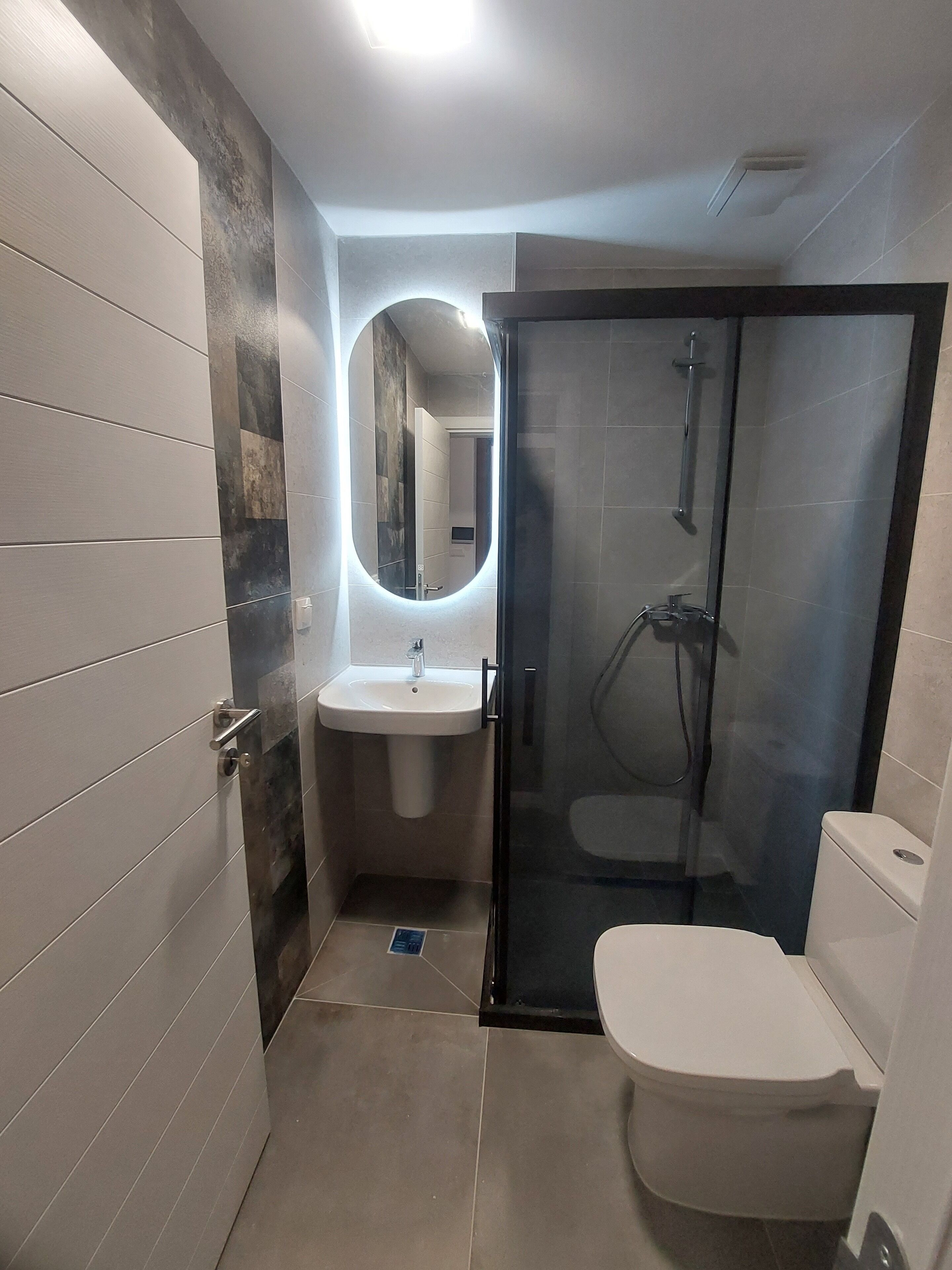A modern bathroom with a glass-enclosed shower, a white sink, and a toilet.