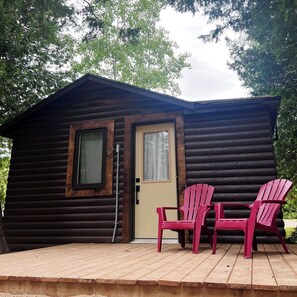 A log cabin with two windows, a door, and a small porch with two Adirondack chairs. - Red Bay Lodge (South Bruce Peninsula)