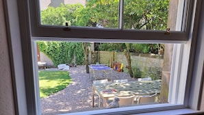 Vista a través de una ventana que muestra un patio trasero con una mesa, sillas, mesa de ping pong y un jardín.