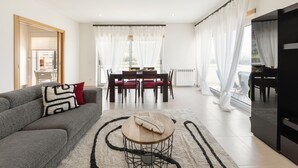 A modern living room with a grey sofa, a wooden coffee table, and a dining area with a table and chairs. - Nazaré Beach House - 5 minutes walking to the beach (Leiria)