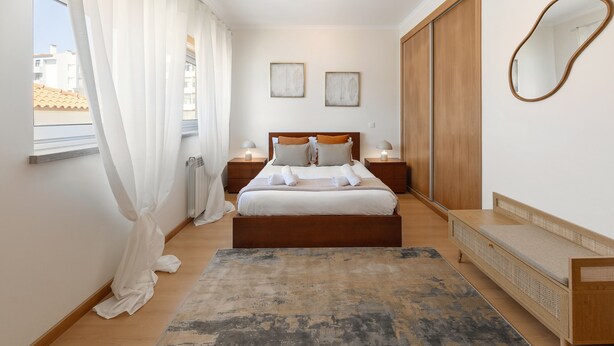 A bedroom with a bed, bedside tables, a mirror, and a view of the outside. - Nazaré Beach House - 5 minutes walking to the beach (Leiria)