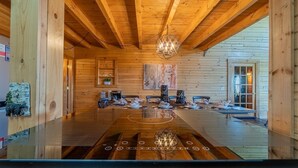 A spacious wooden interior with a large dining table, wooden beams, and a chandelier. - Luxe Amish Log Cabin | 10 Acres | Private Pond | Kayak | Pizza Oven | ATV Trails (Stratford)