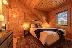 A wooden cabin bedroom with a bed, nightstands, a dresser, and a window with blinds.