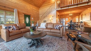A spacious wooden cabin interior with a large living area, a dining area, and a staircase leading to an upper level. - Luxe Amish Log Cabin | 10 Acres | Private Pond | Kayak | Pizza Oven | ATV Trails (Stratford)